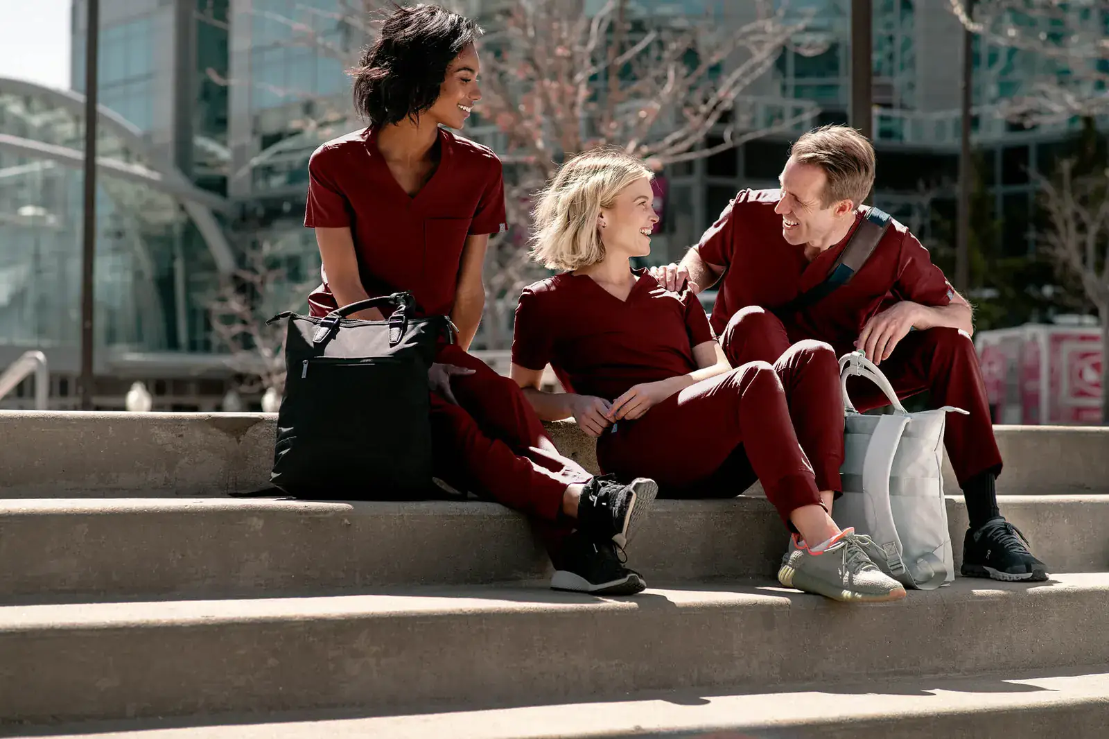 Three healthcare professionals in Merlot Red MedTailor scrubs sitting on city steps